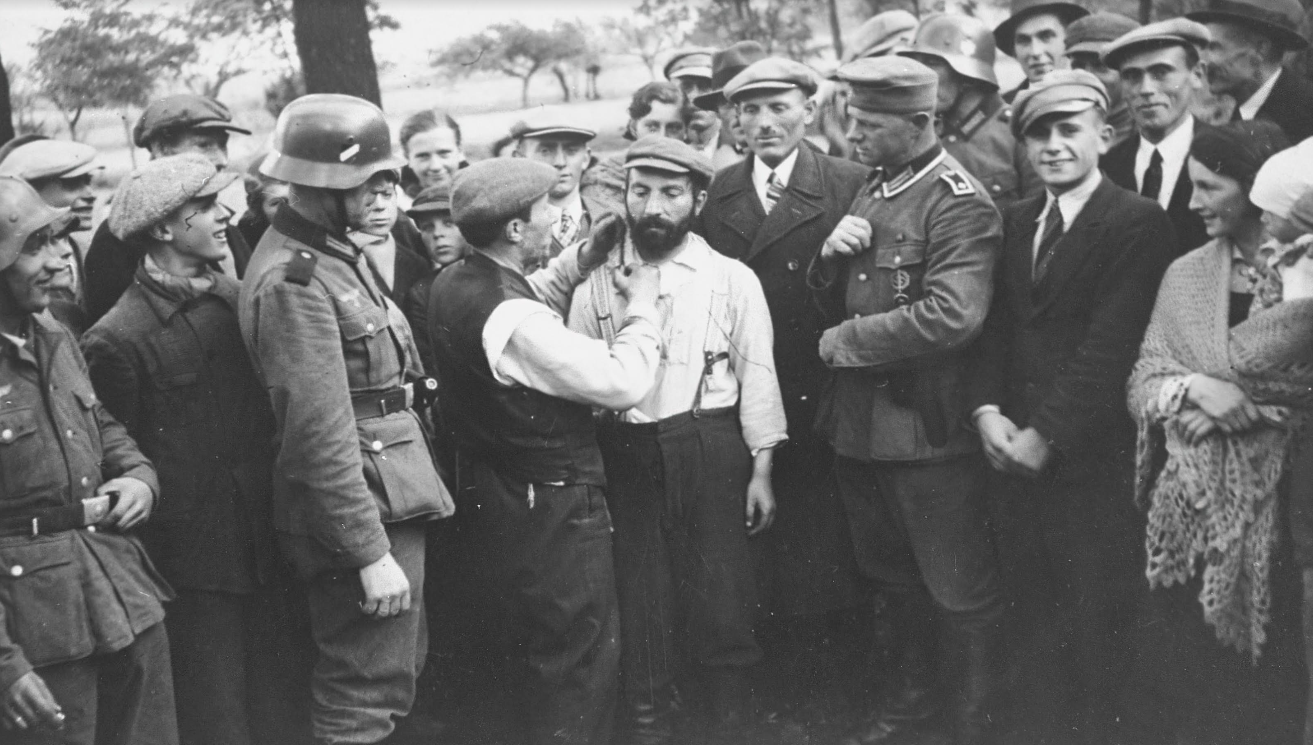 A group of German soldiers and civilians look on as a Jewish man is forced to cut the beard of another in Tomaszow Mazowiecki in 1939